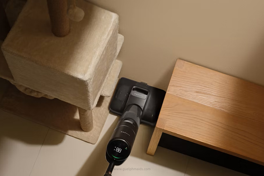 Cordless vacuum cleaner cleaning the floor beside a cat scratching post and wooden table.